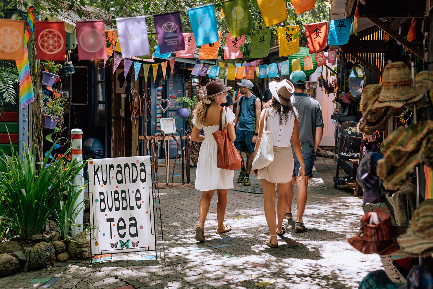 four tourists walking through Kuranda Markets surrounded by stalls and coloured flags
